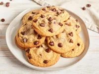 A plate of chocolate chip cookies with chocolate morsels scattered around on cloth napkins.