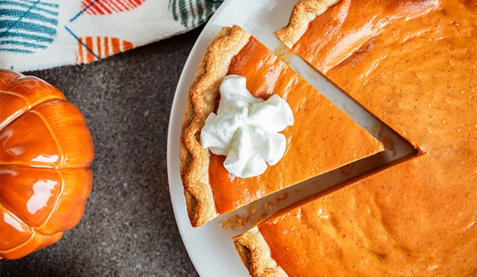 Vista aérea de un pastel de calabaza Libby's en un plato con una porción cortada, una servilleta y una calabaza de adorno.