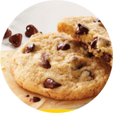 Imagen circular de cerca de dos galletas con trocitos de chocolate apiladas junto a trozos más grandes.