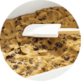 Imagen circular de una espátula en una placa con masa de galletas extendida.