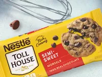 Un paquete de bocaditos semidulces Nestlé Toll House con un batidor y un bocadito de chocolate sobre la mesa de mármol.